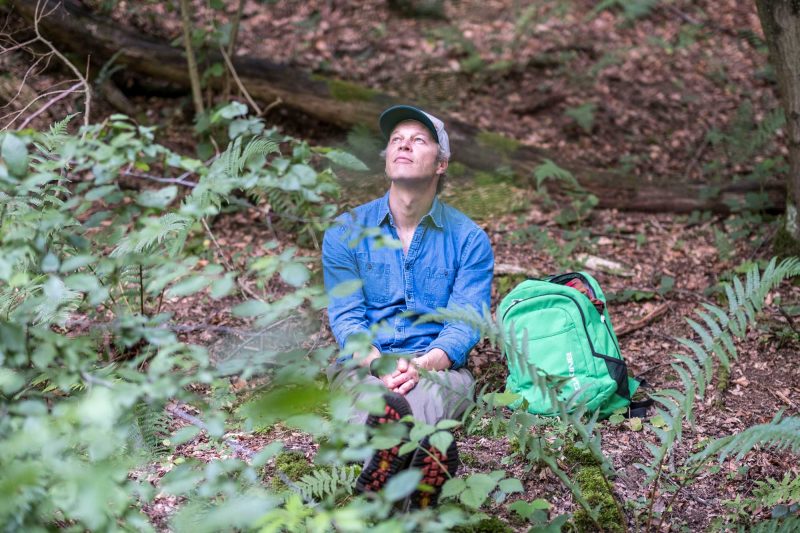 Seminarleiter Tom Haass genießt das Waldbaden und sitzt auf dem mit Laub bedeckten Waldboden.