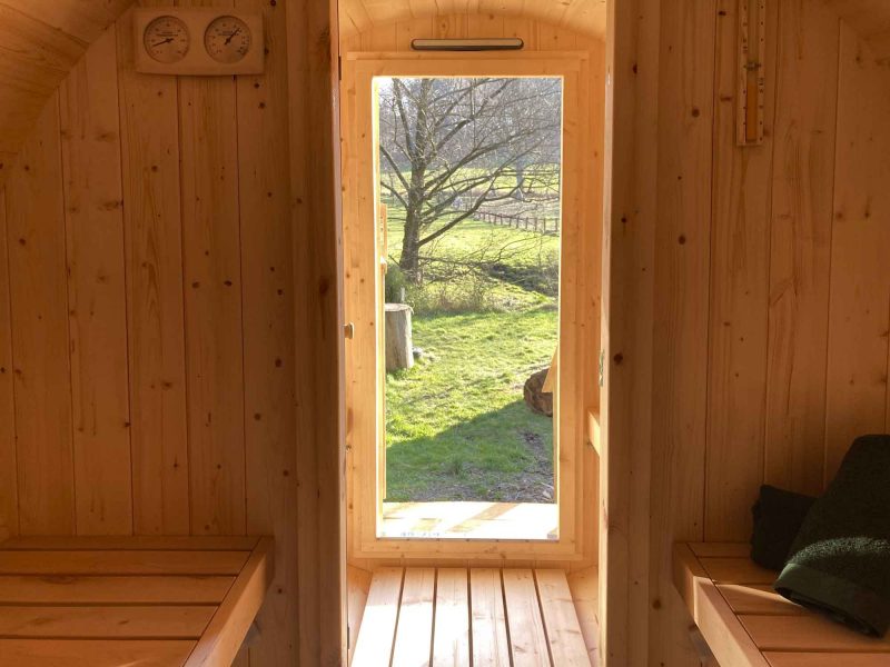 Blick durch die gläserne Tür aus der gemütlichen Fass Sauna nach draussen in die schöne Natur.